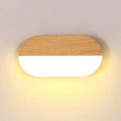Vue frontale applique murale LED ovale bois clair grain fin sur fond crème, contraste acrylique translucide