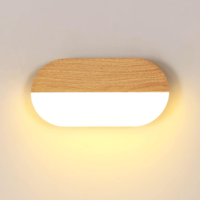 Vue frontale applique murale LED ovale bois clair grain fin sur fond crème, contraste acrylique translucide