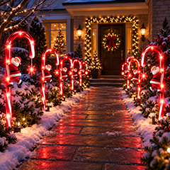 Des cannes à sucre lumineuses bordent une allée enneigée devant une maison décorée pour Noël.